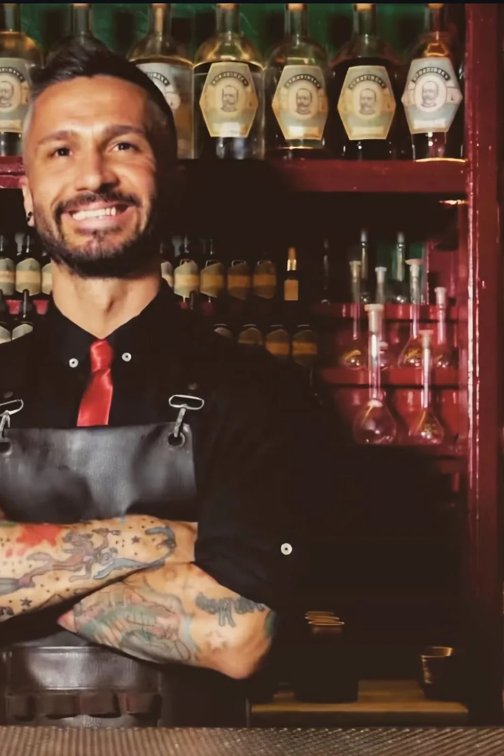 Bartender dello staff sorridente con le braccia incrociate davanti alla bottigliera